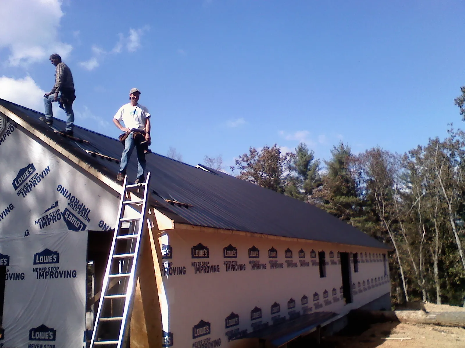 Two roofers standing on a long dark metal roof over a wrapped building in Camden