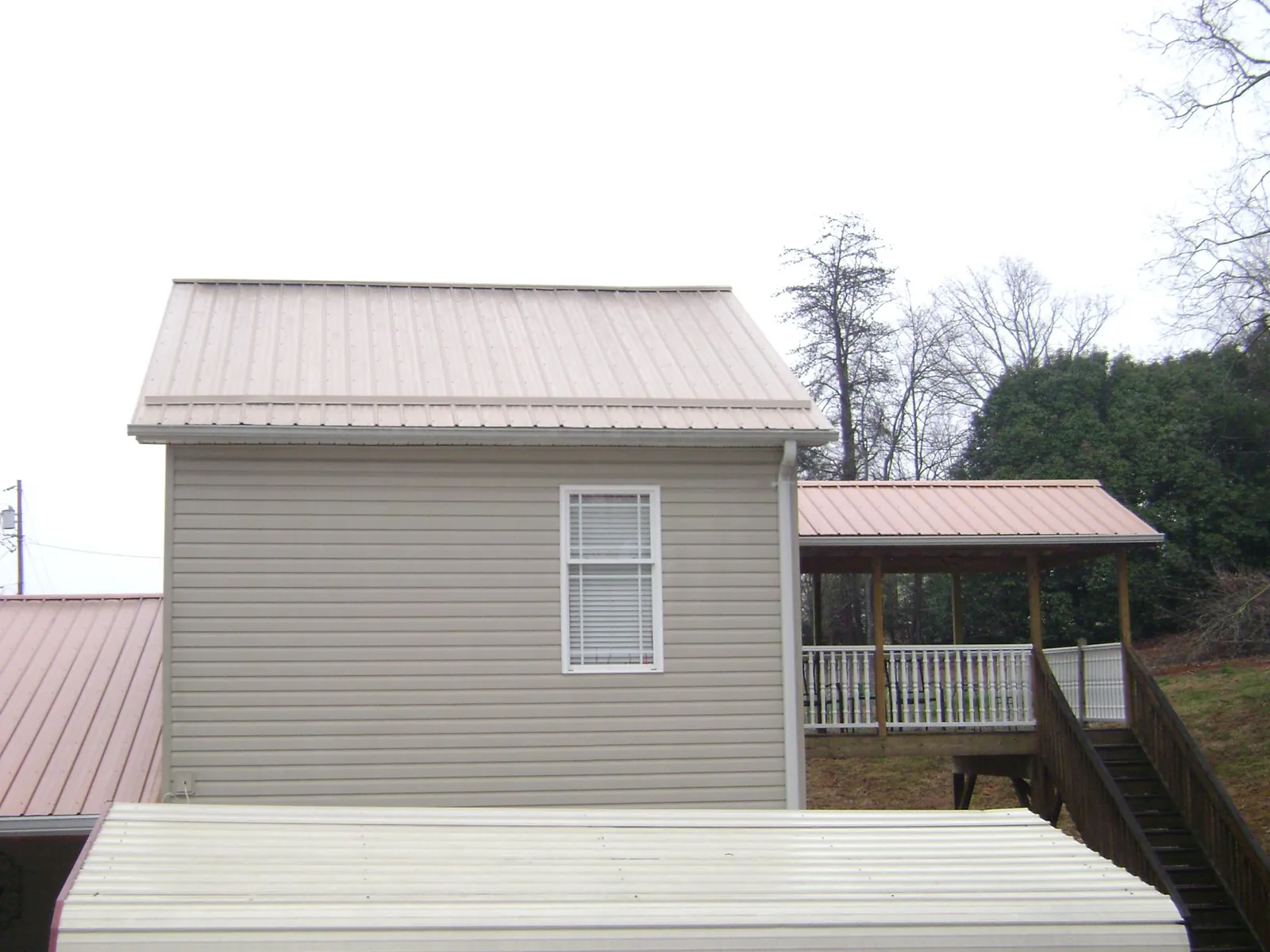 Tan metal roofs on a two story addition and attached porch, from a Roof Replacement job in Camden